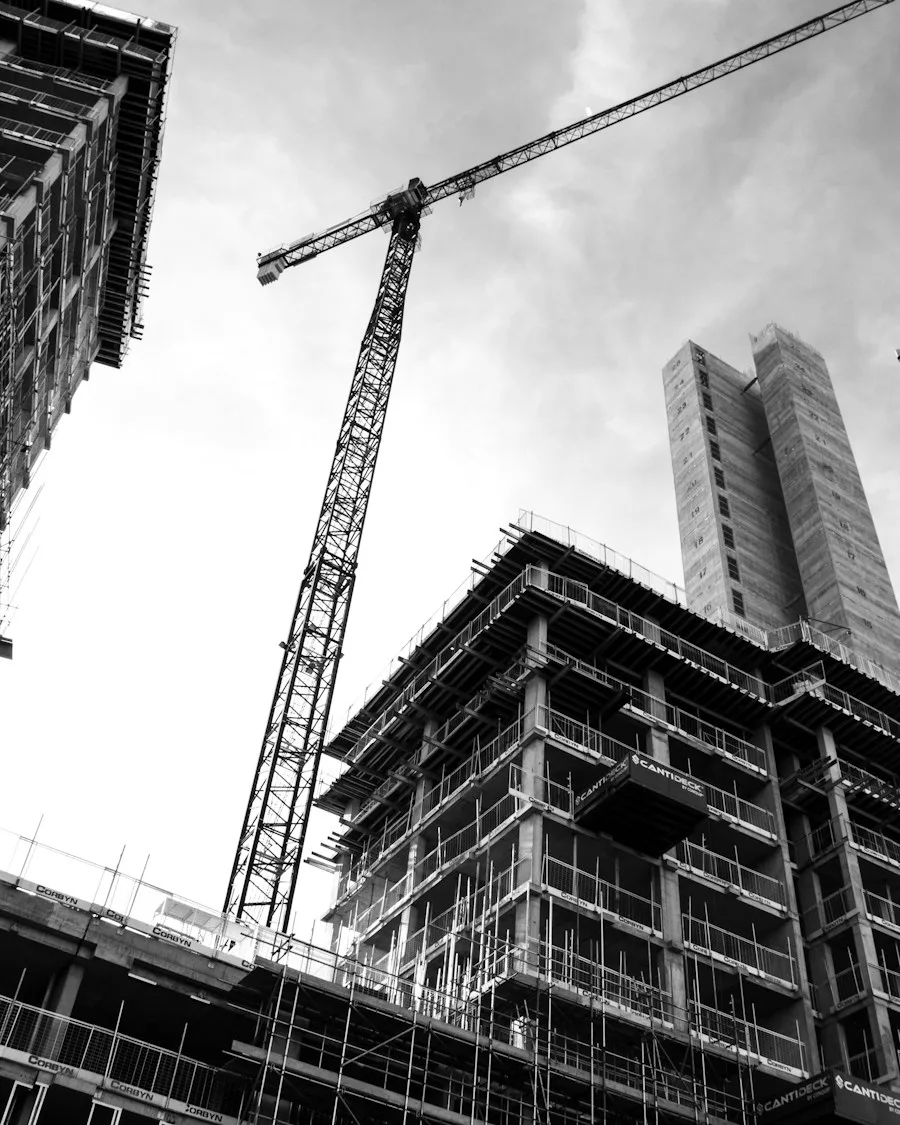 Grayscale photo of a crane in front of a building under construction